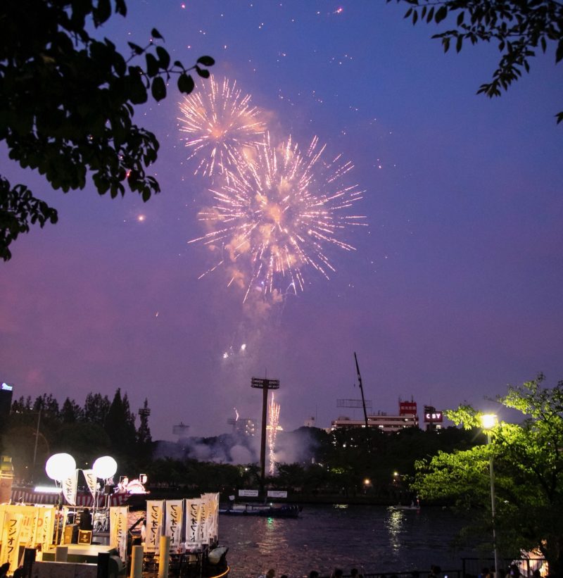 fireworks over the Okawa River at Tenjin Matsuri summer festival with boat in foreground