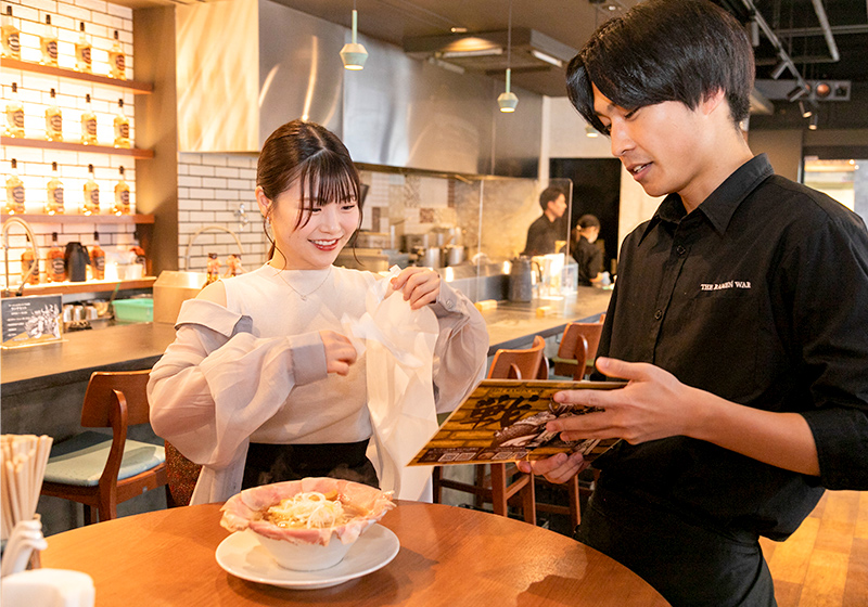 Yuina Deguchi from NMB48 talking with server about menu at The Ramen War