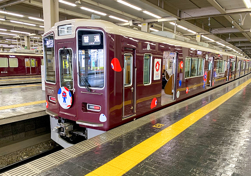 阪急電車の万博ラッピング車両は、ベースのマルーンカラーを残したデザイン